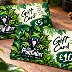 Two Frogfather digital gift cards displayed on a desk, featuring the Frogfather logo and tropical leaf designs.